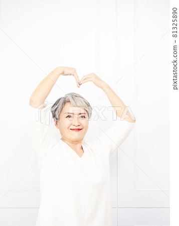 A mature, beautiful, gray-haired woman with a gray hair, a closed sleeve, and a hand-shaped heart-shaped sign with a smile on her face. Romantic concept. A mature, beautiful, gray-haired woman with a gray hair, a closed sleeve, and a hand-shaped heart-shaped sign with a smile on her face. Romantic concept. 81325890