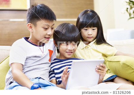three asian children sitting on couch at home playing video game using digital tablet 81326206