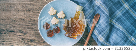 Maple syrup bottle and pure soft sugar candy and taffy top view on kitchen table panoramic banner. Cooking ngredient for desssert recipe, traditonal food from Quebec wood rustic plate panorama 81326523