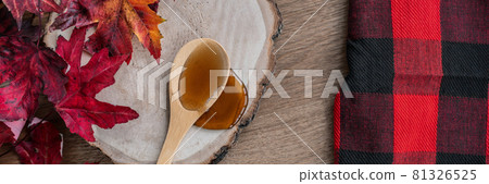Maple syrup sweet ingredient for desssert recipes, liquid dripping from wooden spoon on wood log rustic sugar shack banner panoramic with buffalo plaid and red leaves Maple syrup sweet ingredient for desssert recipes, liquid dripping from wooden spoon on wood log rustic sugar shack banner panoramic with buffalo plaid and red leaves 81326525