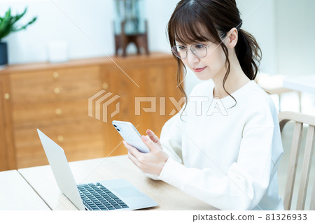 A woman with glasses who operates a smartphone while using a laptop in the living room A woman with glasses who operates a smartphone while using a laptop in the living room 81326933