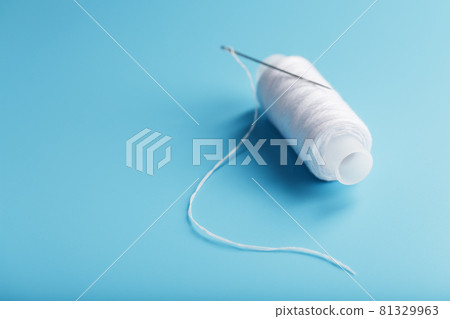 A spool of white thread with a needle on a blue background. 81329963