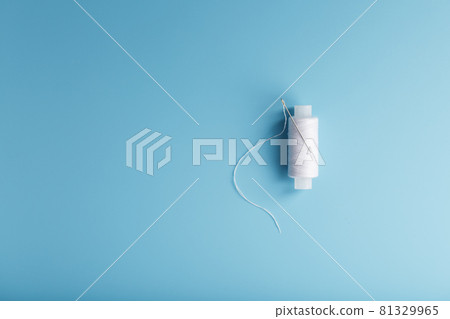 A spool of white thread with a needle on a blue background. 81329965