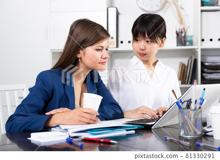 Businesswomen discussing over laptop at desk Businesswomen discussing over laptop at desk 81330291