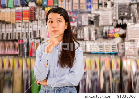 Portrait of Asian girl having doubts about choice of goods in cosmetics store Portrait of Asian girl having doubts about choice of goods in cosmetics store 81330306