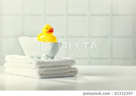 A miniature bubble bath, yellow rubber duck and white towels on bathroom countertop, children bath accessories, baby care 81332397