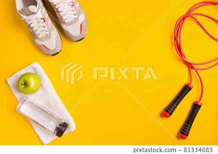 Athlete's set with female clothing, skipping rope and bottle of water on yellow background 81334083