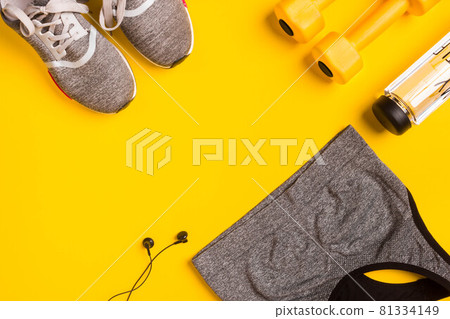 Fitness accessories on a yellow background. Sneakers, bottle of water, headphones and sport top. Fitness accessories on a yellow background. Sneakers, bottle of water, headphones and sport top. 81334149