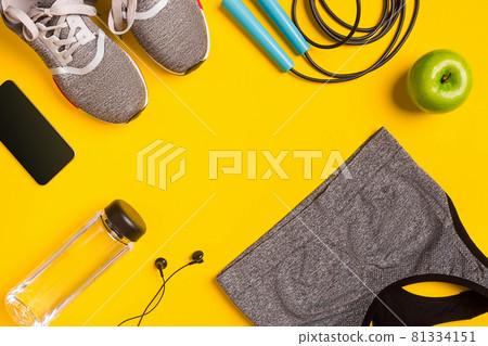 Fitness accessories on yellow background. Sneakers, bottle of water, headphones and sport top. Fitness accessories on yellow background. Sneakers, bottle of water, headphones and sport top. 81334151