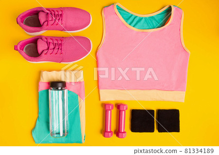 Fitness accessories on yellow background. Sneakers, bottle of water, dumbbells and sport top. 81334189
