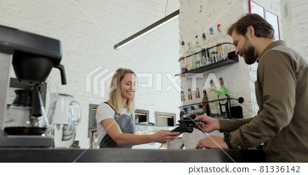 Handsome bearded man paying for takeaway coffee with mobile phone at coffee shop. Worker serving a customer who uses smartphone to pay in coffee shop. Handsome bearded man paying for takeaway coffee with mobile phone at coffee shop. Worker serving a customer who uses smartphone to pay in coffee shop. 81336142