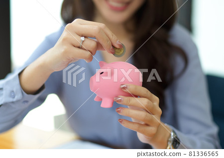 Beautiful woman holding and putting coin in piggy bank Beautiful woman holding and putting coin in piggy bank 81336565
