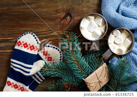 Two cups of hot cocoa or chocolate with marshmallow, mittens, christmas decor and fir tree on wooden rustic background from above. 81336725