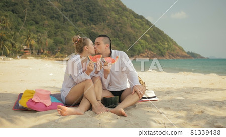 The cheerful love couple holding and eating slices of watermelon on tropical sand beach sea. Romantic lovers two people spend summer weekend. 81339488