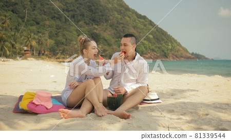 The cheerful love couple holding and eating slices of watermelon on tropical sand beach sea. Romantic lovers two people spend summer weekend. The cheerful love couple holding and eating slices of watermelon on tropical sand beach sea. Romantic lovers two people spend summer weekend. 81339544