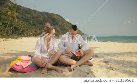 The cheerful love couple holding and eating slices of watermelon on tropical sand beach sea. Romantic lovers two people spend summer weekend. The cheerful love couple holding and eating slices of watermelon on tropical sand beach sea. Romantic lovers two people spend summer weekend. 81339568
