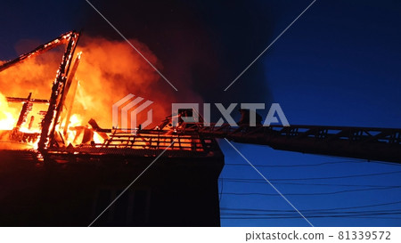 The roof of the house is on fire. The residential building burn, village. Firefighters put out a fire from the crane from above. Smoke and sparks. 81339572