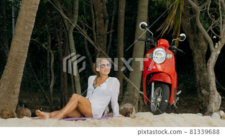 Scooter road trip. Woman alone on red motorbike in white clothes on sand beach by ocean. One girl caucasian tourist walk near tropical palm tree. Scooter road trip. Woman alone on red motorbike in white clothes on sand beach by ocean. One girl caucasian tourist walk near tropical palm tree. 81339688