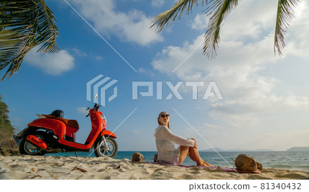 Scooter road trip. Woman alone on red motorbike in white clothes on sand beach by ocean. One girl caucasian tourist walk near tropical palm tree. 81340432