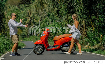 Love couple on red motorbike in white clothes, sunglasses on forest road trail trip. Dancing road. Two caucasian tourist woman man dance near scooter. Love couple on red motorbike in white clothes, sunglasses on forest road trail trip. Dancing road. Two caucasian tourist woman man dance near scooter. 81340440