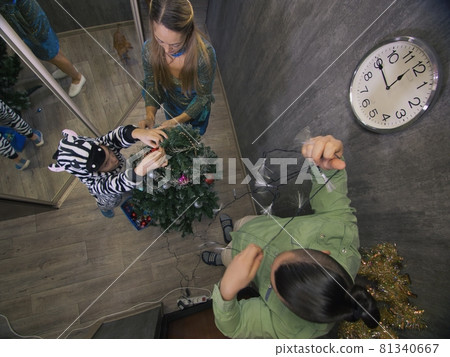 The family fast and fanny decorates the Christmas tree. Top view. Time on the clock is 23.45 on wall. Happy dad, mom, daughter are run around tree. 81340667