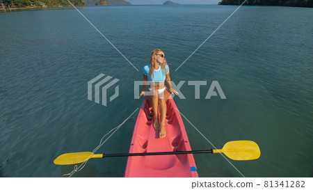Pretty slim woman in elegant swimsuit lies in pink plastic kayak drifting on azure ocean at exotic resort upper view. Pretty slim woman in elegant swimsuit lies in pink plastic kayak drifting on azure ocean at exotic resort upper view. 81341282