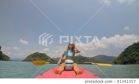 Sportive woman rows pink plastic canoe along sea water. Positive sports girl hand padding on kayak, front view. Sportive woman rows pink plastic canoe along sea water. Positive sports girl hand padding on kayak, front view. 81341357