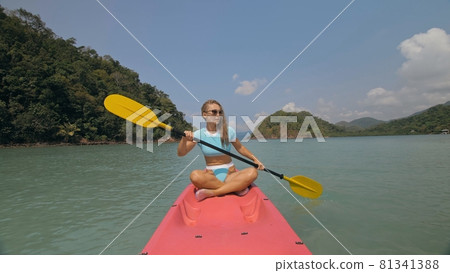 Sportive woman rows pink plastic canoe along sea water. Sportive woman rows pink plastic canoe along sea water. 81341388