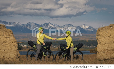 The man and woman travel on mixed terrain cycle touring with bikepacking. The two people journey with bicycle bags. Mountain snow capped, stone arch. The man and woman travel on mixed terrain cycle touring with bikepacking. The two people journey with bicycle bags. Mountain snow capped, stone arch. 81342042