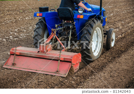 The tractor is cultivating the soil in the farm field. Freeing milling earth ground from old crops. Softening and improving soil qualities. Farming. Preparatory earthworks. Agriculture agribusiness The tractor is cultivating the soil in the farm field. Freeing milling earth ground from old crops. Softening and improving soil qualities. Farming. Preparatory earthworks. Agriculture agribusiness 81342043
