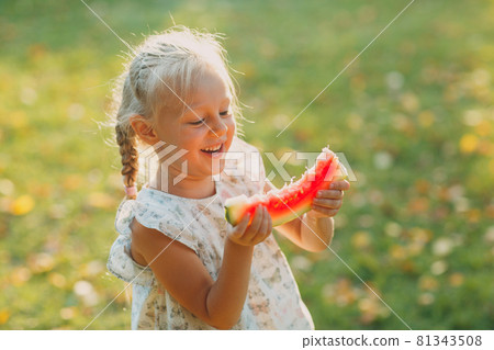Cute blond little girl with watermelon on the grass in park Cute blond little girl with watermelon on the grass in park 81343508