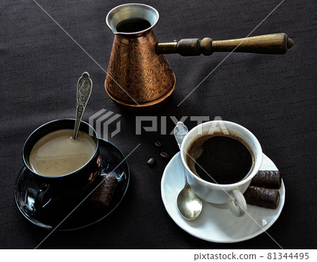 Coffee theme. Two cups of coffee and a jezva on the table. A white cup with black coffee and a black cup with coffee with milk. Coffee theme. Two cups of coffee and a jezva on the table. A white cup with black coffee and a black cup with coffee with milk. 81344495