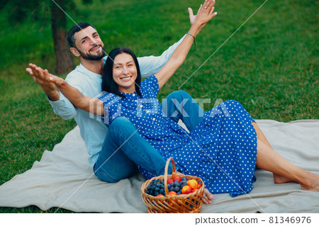 Young adult woman and man couple picnic at green grass meadow in park with open arms Young adult woman and man couple picnic at green grass meadow in park with open arms 81346976