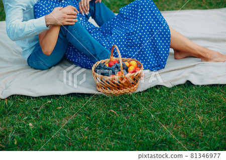 Young adult woman and man couple picnic at green grass meadow in park with fruits in basket Young adult woman and man couple picnic at green grass meadow in park with fruits in basket 81346977