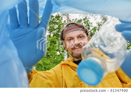 Waving hello invites you to join cleaning park. Volunteer collecting litter picking up trash in garbage bag. Volunteer cleaning forest view from inside a plastic bag. Picking up garbage in plastic bag 81347490