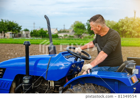 A farmer is driving a tractor. Agro industry, agribusiness. Farming, agriculture. Countryside farmland. Small farms. Work in the agricultural industry. 81349554