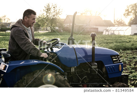 Farmer driving a tractor across the field. Agro industry, agribusiness. Farming, agriculture. Countryside farmland. Small farms. Work in the agricultural industry. 81349584