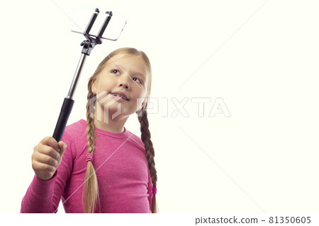 Cute little caucasian girl taking a photo using a modern smartphone on a white background. Selfie stick 81350605
