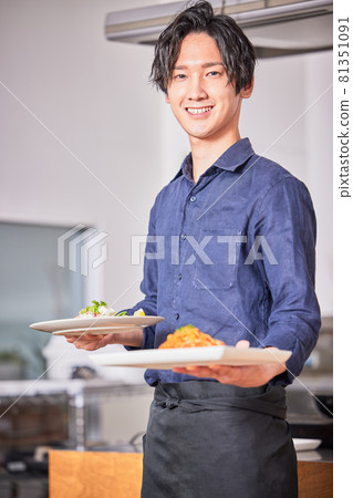 Image of a young man in an apron carrying food 81351091