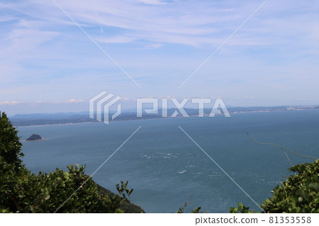 The blue sea with white waves with a small round island overlooking the green trees, the mountains and towns on the opposite bank, the thin clouds and the blue sky The blue sea with white waves with a small round island overlooking the green trees, the mountains and towns on the opposite bank, the thin clouds and the blue sky 81353558