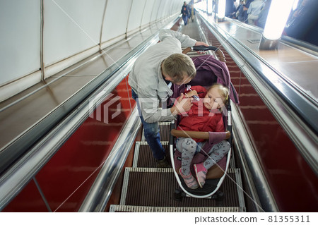 Child in perambulator with father on escalator in underground. 81355311