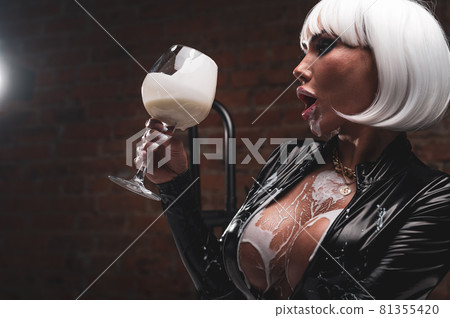 Sexy woman in short white wig and latex suit drinks milk from a glass. 81355420