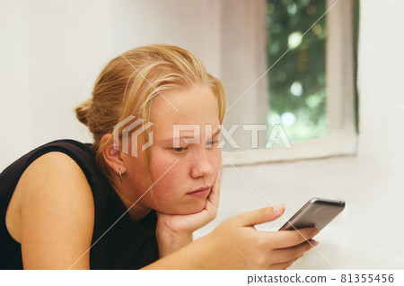 Teen girl holds a mobile phone in her hand and looks at the screen Teen girl holds a mobile phone in her hand and looks at the screen 81355456