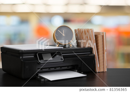 Compact home printer on desk with books against blurred background 81356365
