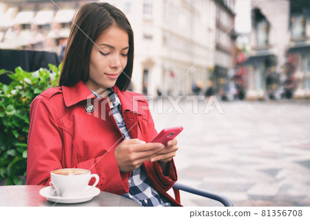 Cafe woman using mobile phone drinking cappuccino coffee at outdoor street european city. Europe travel lifestyle. Asian businesswoman in fashion red trench coat Cafe woman using mobile phone drinking cappuccino coffee at outdoor street european city. Europe travel lifestyle. Asian businesswoman in fashion red trench coat 81356708