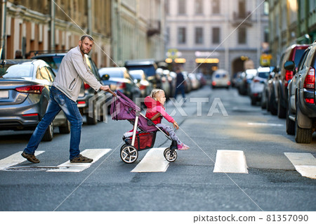 Father drives child in perambulator along pedestrian crossing. 81357090