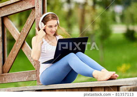 Woman in wireless headphones works using laptop outside. Woman in wireless headphones works using laptop outside. 81357113