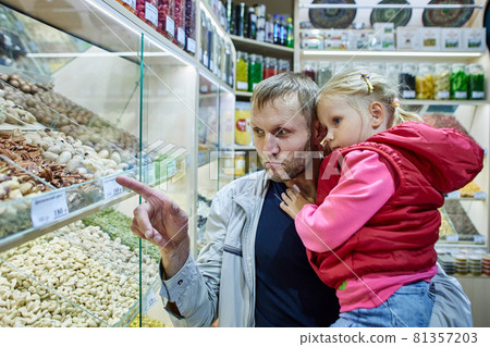 Father is holding little girl near stand with nuts in marketplace. 81357203