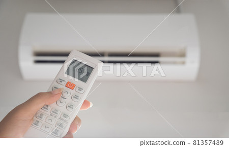 Hand holding remote controller directed on the air conditioner inside the room and set at ambient temperature,25 degrees celsius. Hand holding remote controller directed on the air conditioner inside the room and set at ambient temperature,25 degrees celsius. 81357489