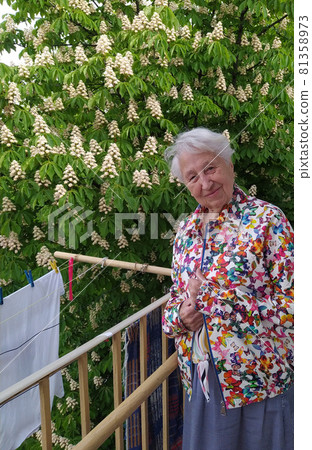 Positive senior woman watering decorative plants on balcony 81358973